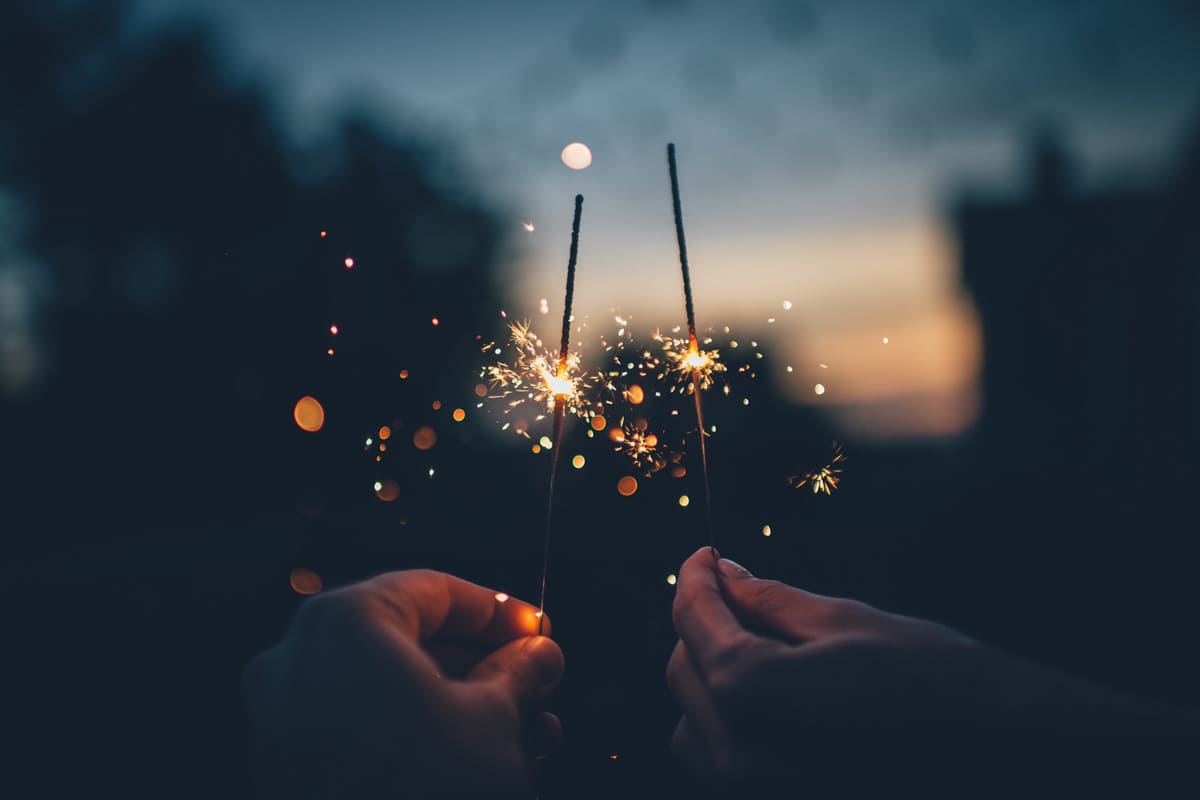 Selbstreflexion zum Jahresende: Zwei Hände halten zwei Wunderkerzen in die Nacht