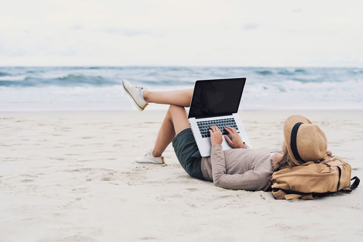 Organisational development - New Work: Young woman on the beach with a laptop on her knees - netzwerk managementberatung | coaching